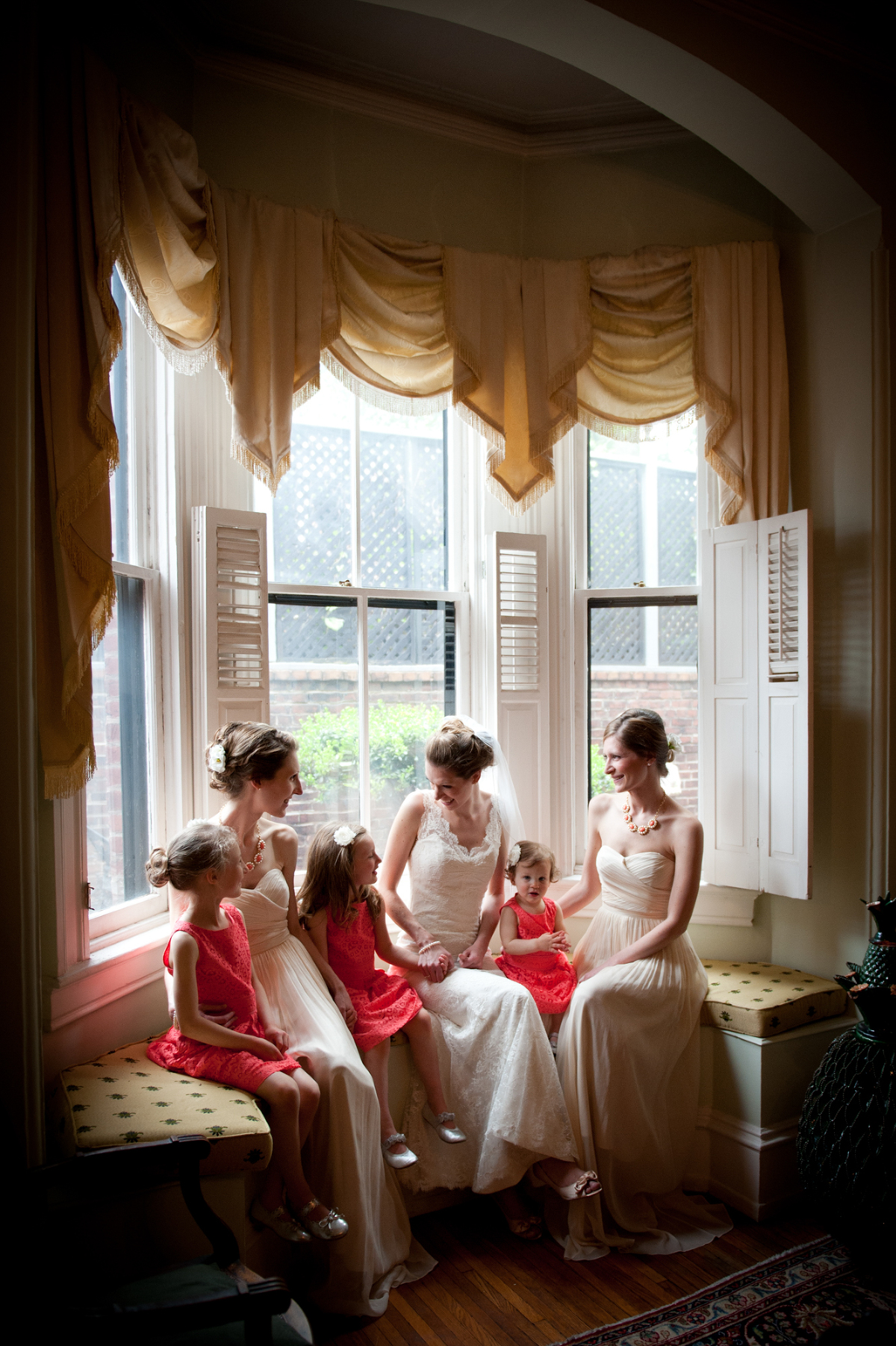 A bride with her 2 sisters and her niece talking on her wedding day in a Bay window.