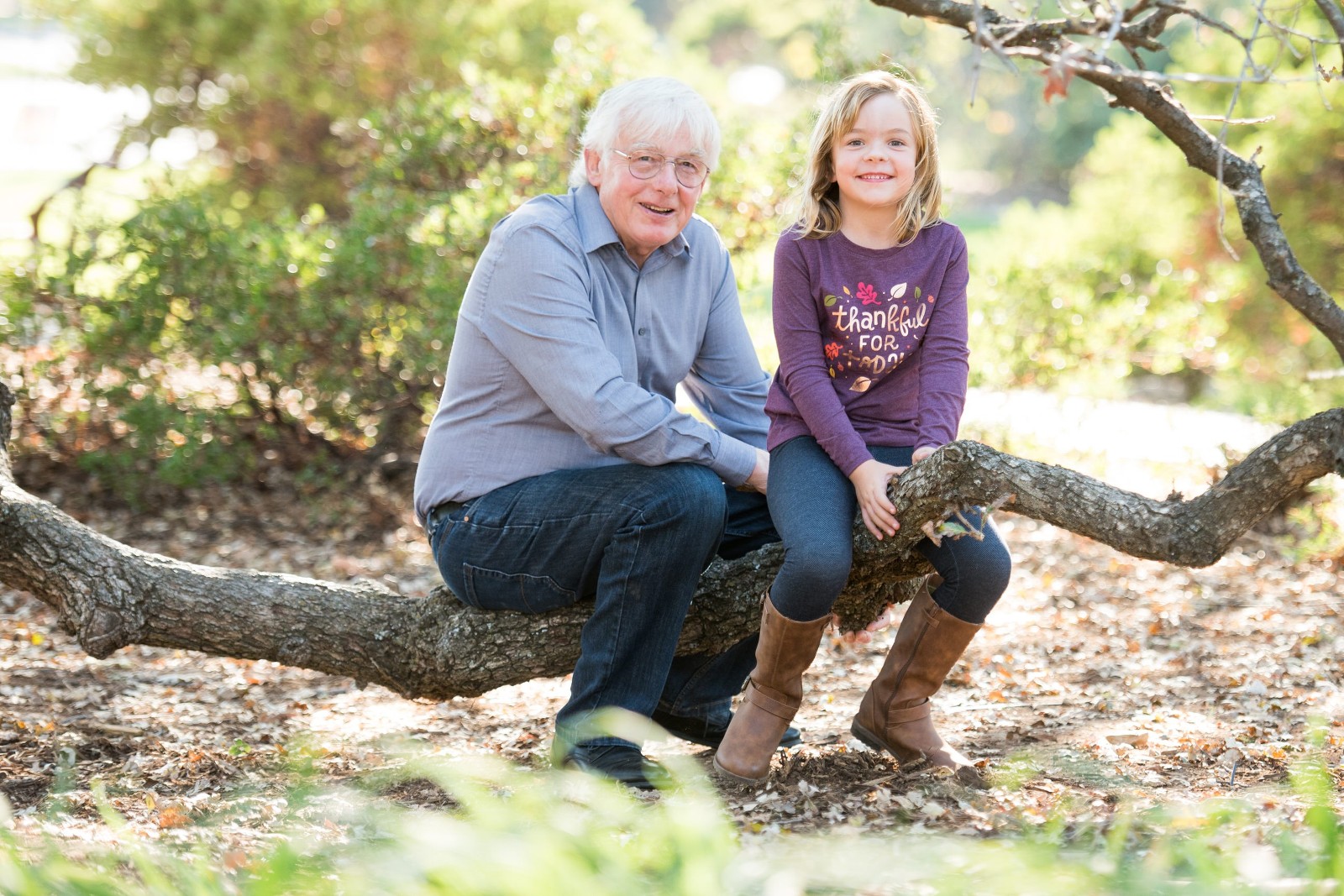 A grandpa and his granddaughter sit on a tree branch together in El Dorado Hills
