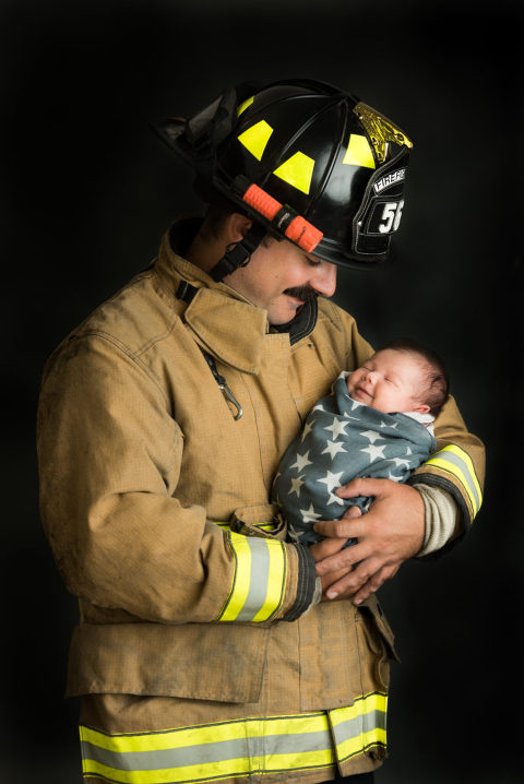 Fireman holds his newborn baby girl who is smiling