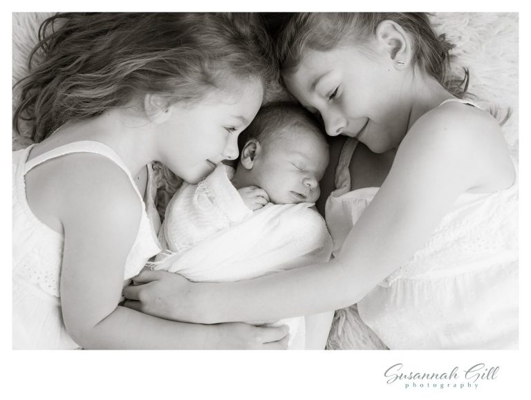 2 little girls snuggle their newborn brother during a photoshoot.